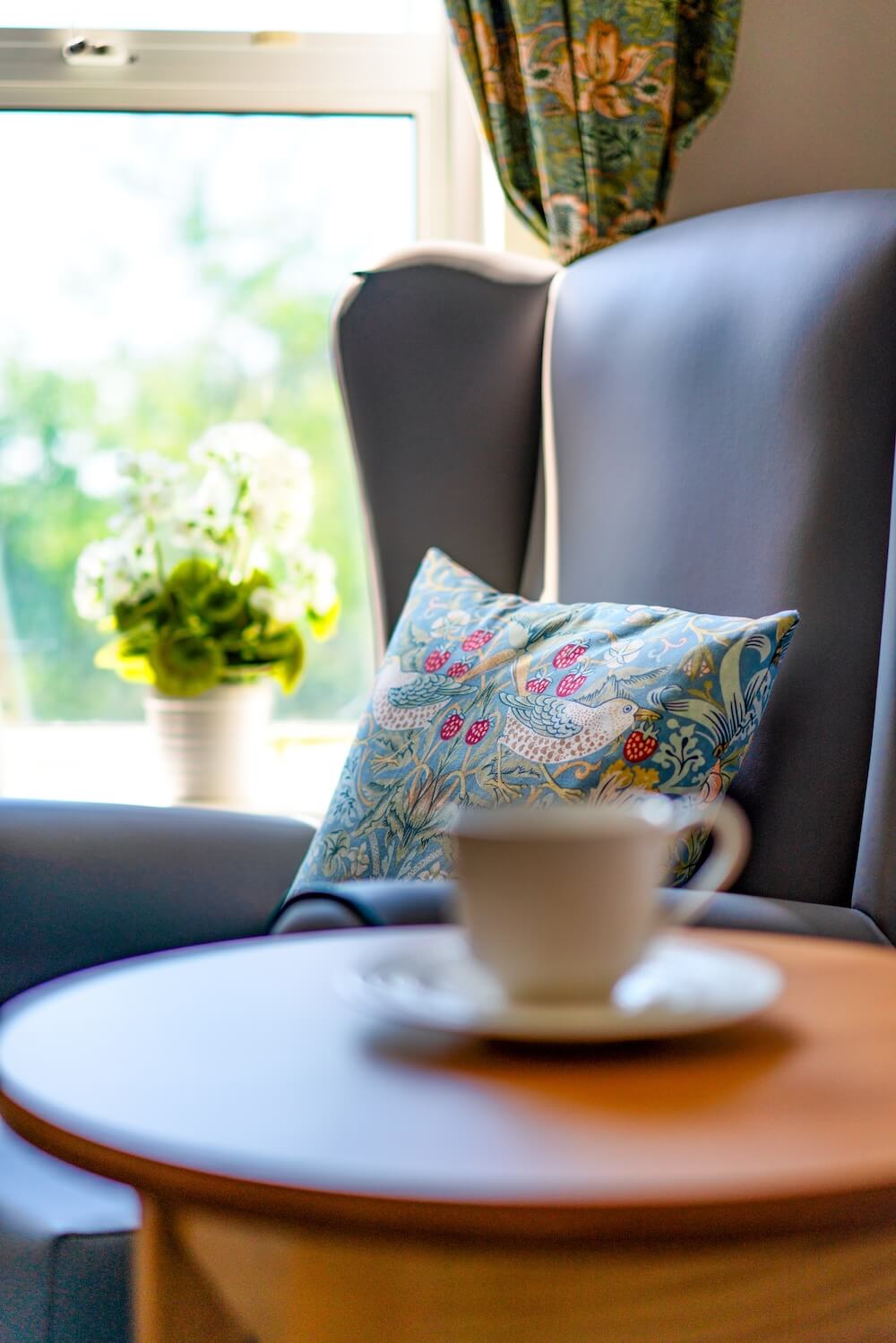 Armchair with a cushion and a teacup on the table beside it.