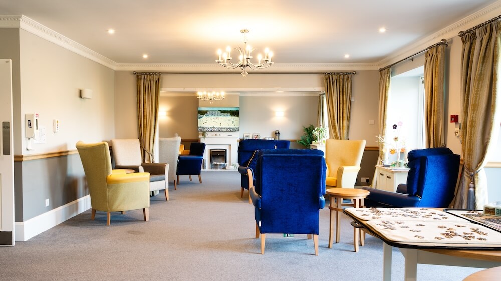 Lounge with navy blue, yellow, and beige armchairs, a table with a puzzle, a fireplace, and a TV.