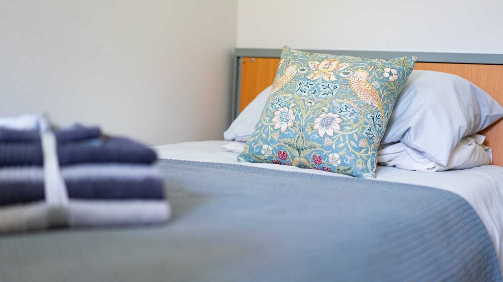 Bed with cushions and a neatly folded set of towels placed on top.